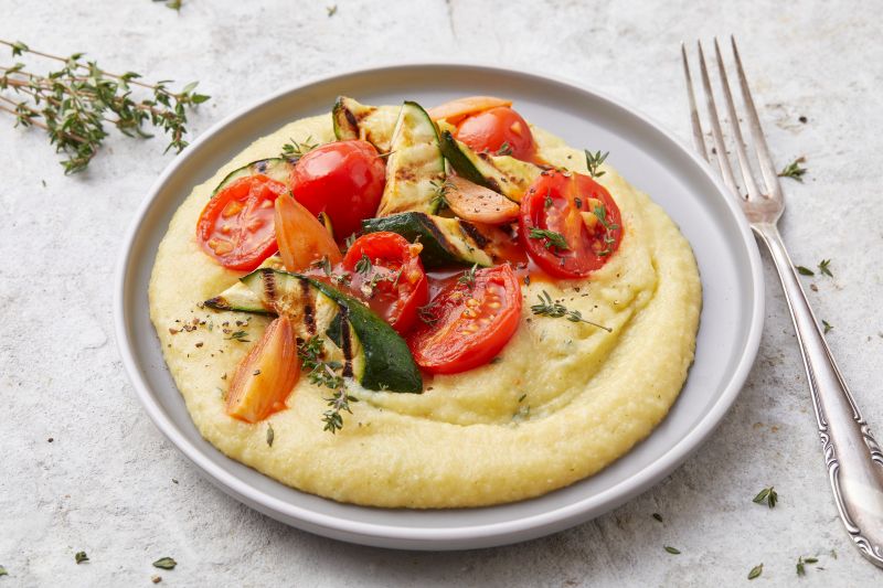 On a Plate, a Circle of Creamy Polenta is Generously Topped With Roasted Veggies. A Fork Waits Nearby