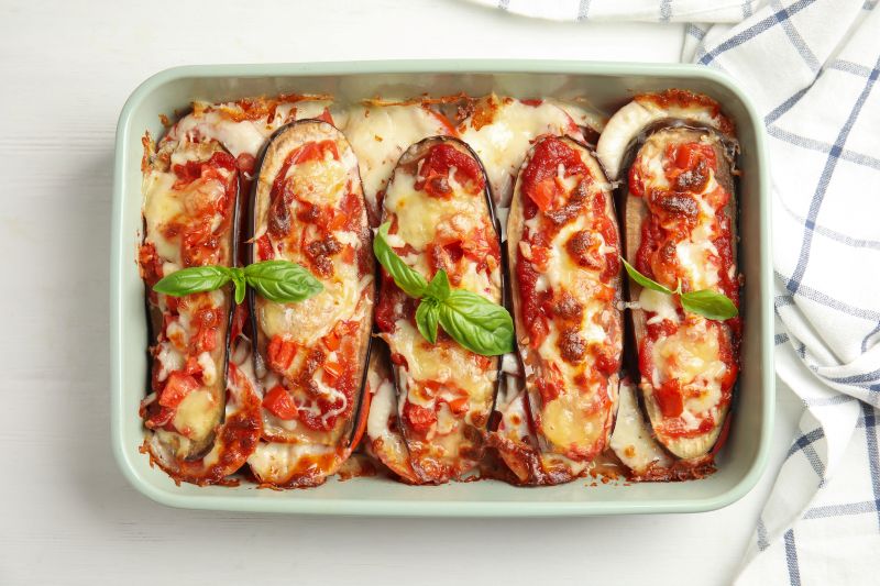 Cheesy, Bubbly Eggplant Pizza Boats in Rectangular Ceramic Baking Dish, Basil Leaves Scattered About on Top