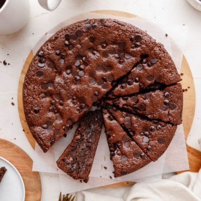 Round Chocolate Espresso Cake Cut into Slices on Round Wooden Cutting Board Surrounded by Plates and Coffee Mugs