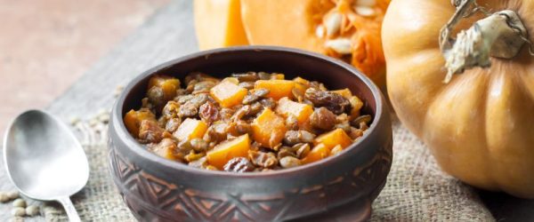 Butternut Squash Lentil Chili in Artistic Round Bowl on Burlap Placemat Next to Whole and Cut Up Squash
