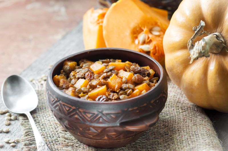 Butternut Squash Lentil Chili in Artistic Round Bowl on Burlap Placemat Next to Whole and Cut Up Squash