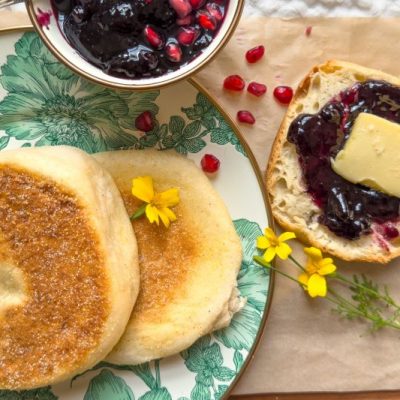 Homemade English Muffins on Fine China. A Sliced Muffin is Slathered with Butter and Jam.