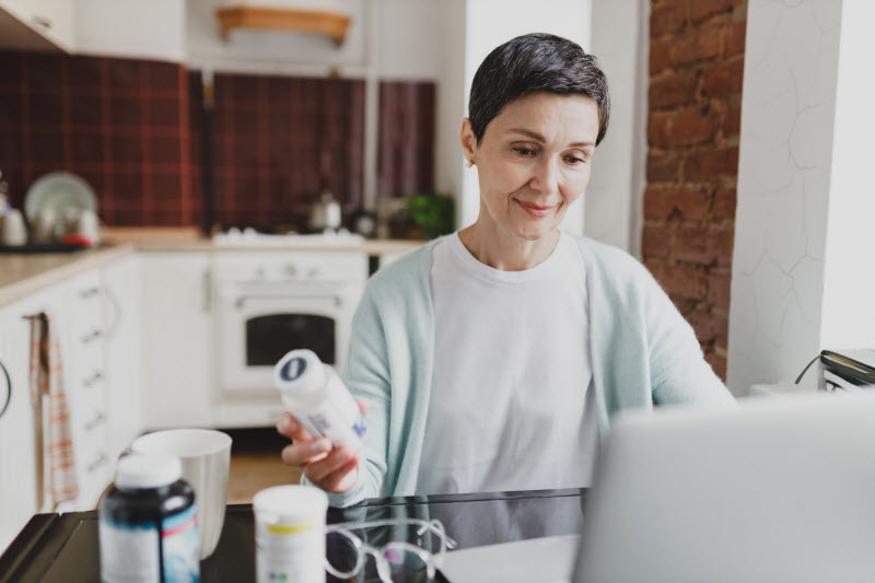 Woman Browsing a Website on Her Laptop in Kitchen to Find the Best Functional Mushroom Supplements 