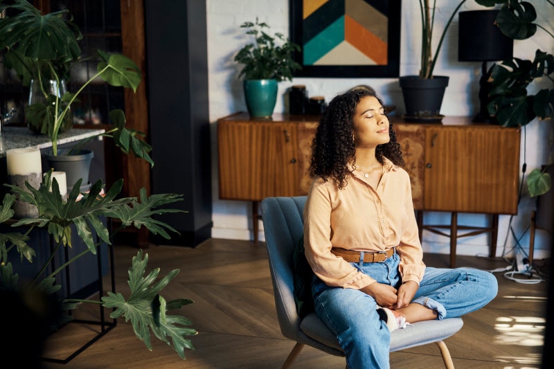 Woman Not Worried About Microplastics in the Air Sitting in Her Living Room Breathing Deeply in Meditation 