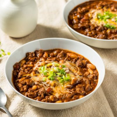 Two Round Bowls of Hearty Ground Turkey Chili Topped with Melted Cheese and Chopped Chives