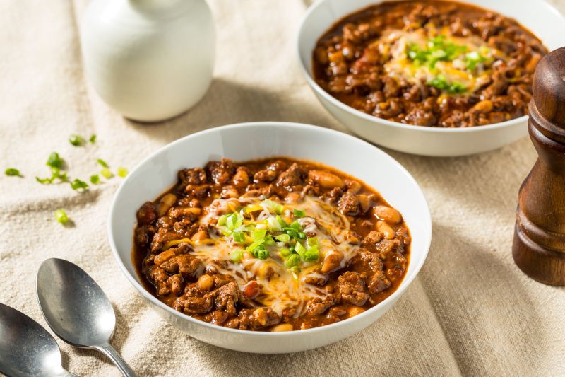 Two Round Bowls of Hearty Ground Turkey Chili Topped with Melted Cheese and Chopped Chives