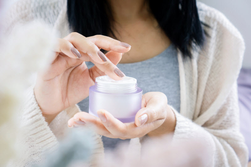 Torso View of Woman Dipping Finger into Tub of Cream to Represent Progesterone Cream Benefits for Menopause