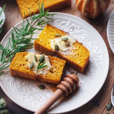 Two Slices of Pumpkin Cornbread Are Topped With Vegan Butter, Pumpkin Seeds and Rosemary.