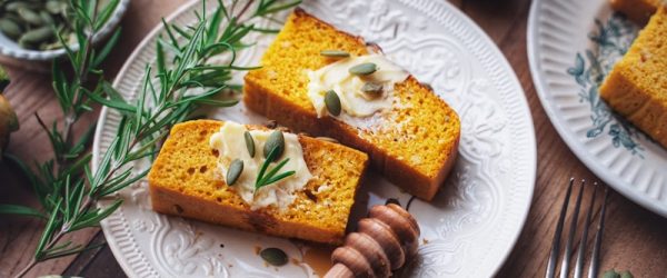 Two Slices of Pumpkin Cornbread Are Topped With Vegan Butter, Pumpkin Seeds and Rosemary.