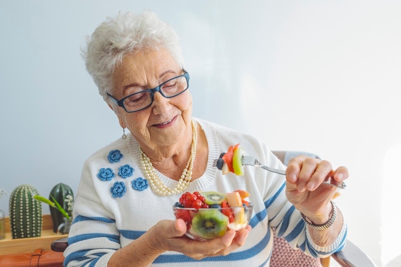 A Senior Woman Enjoys a Fruit Bowl, Representing Snacks for Seniors.