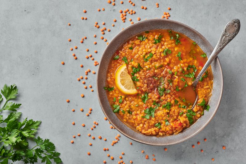 Spicy Lentil Soup with Lime Wedge and Parsley in Big Round Bowl on Countertop Strewn with Red Lentils