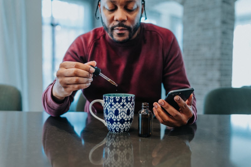 Man Sitting at Table Dropping Herbal Supplement Into Mug of Tea to Support His Body's Stress and Immunity Response
