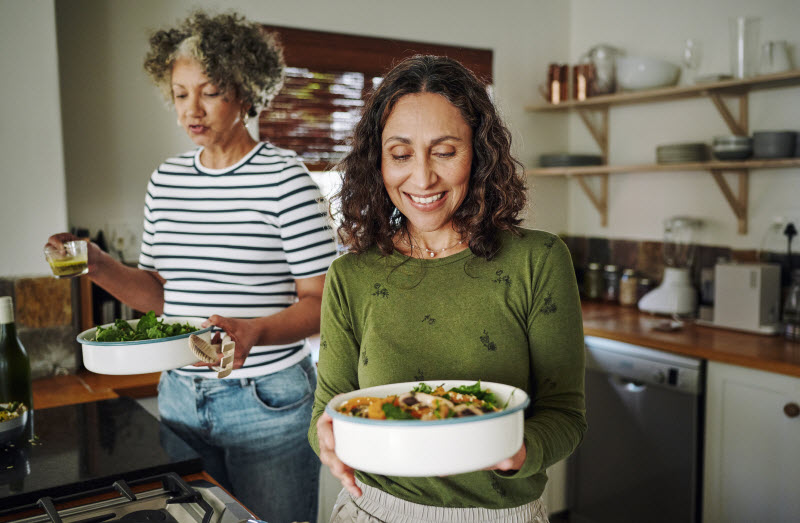 Happy Women Following Menopause Diet Carrying Prepped Casseroles to Dinner Table