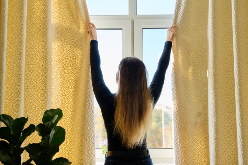 13 Sustainability Tips for an Easy Transition to Greener Living Back View of Woman Closing Curtains While Practicing Easy Sustainability Tips