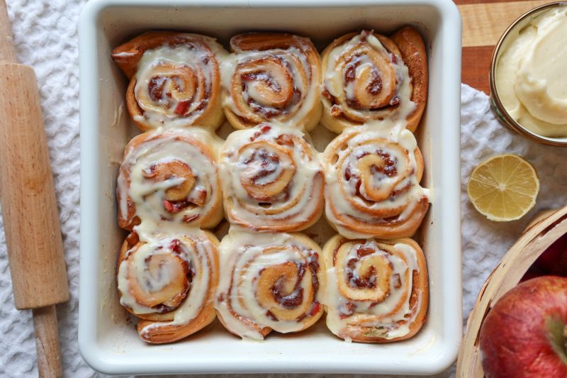 Glazed Apple Cinnamon Rolls in Square Baking Dish on Table Strewn with Apples and Lemons