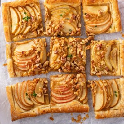 A Sliced Walnut-Topped Apple Tart With Rose-Saffron Syrup on Parchment Paper Surrounded by Apples