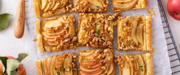 A Sliced Walnut-Topped Apple Tart With Rose-Saffron Syrup on Parchment Paper Surrounded by Apples