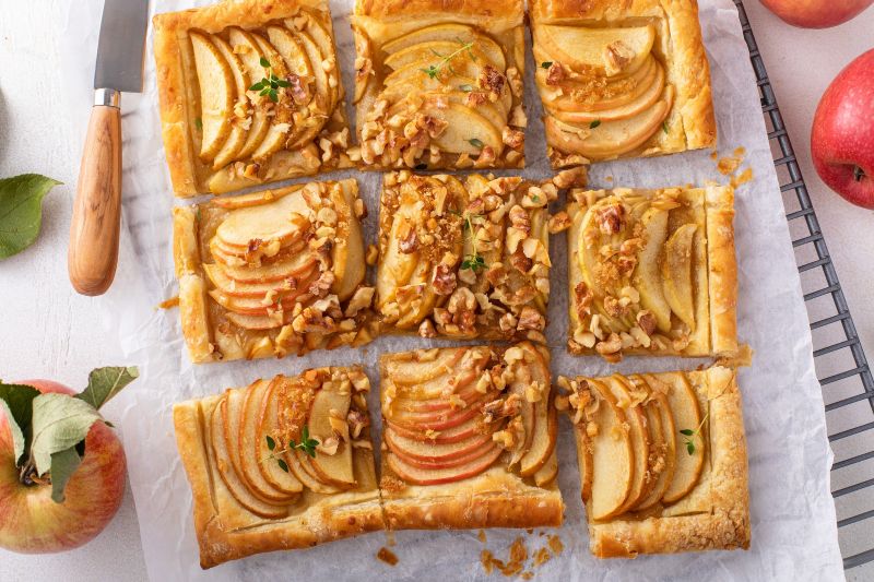 A Sliced Walnut-Topped Apple Tart With Rose-Saffron Syrup on Parchment Paper Surrounded by Apples