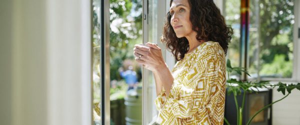 Breast Cancer and Menopause - 5 Facts That Matter for Your Health Pensive-Looking 50-Year-Old Woman Looking Out Living Room Window Wondering About the Connection Between Breast Cancer and Menopause