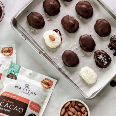 Chocolate-Covered Coconut Candy Bars on Baking Sheet Next to Packages of Navitas Organics Cacao Wafers