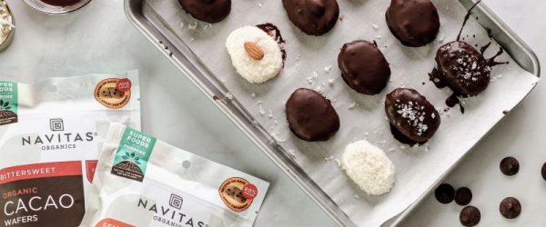 Chocolate-Covered Coconut Candy Bars on Baking Sheet Next to Packages of Navitas Organics Cacao Wafers