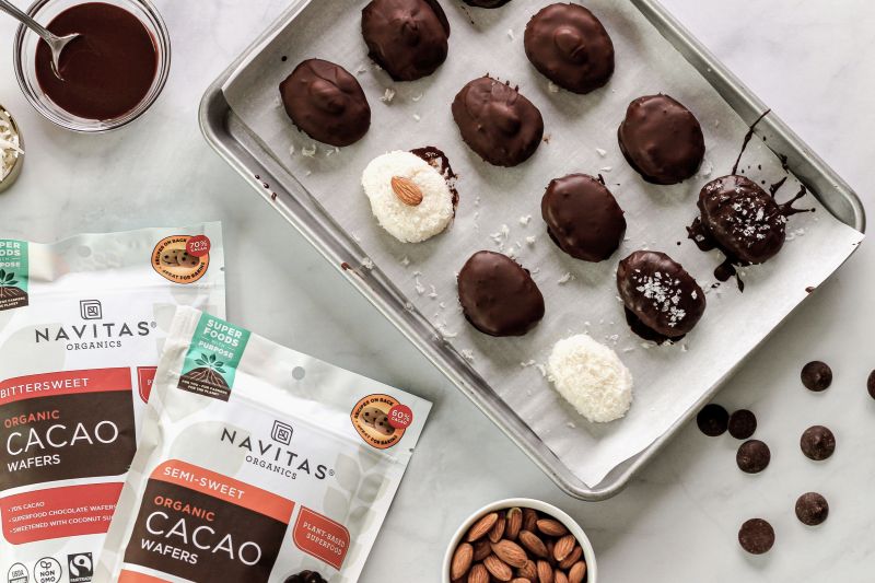 Chocolate-Covered Coconut Candy Bars on Baking Sheet Next to Packages of Navitas Organics Cacao Wafers