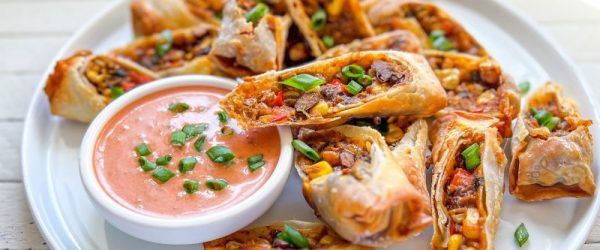 Diagonally Sliced Vegan Southwestern Egg Rolls Filled with Corn, Black Beans, Lentils, Diced Red Peppers & Scallions Surround a Bowl of Salsa-Ranch Dipping Sauce