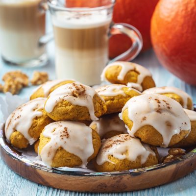 Plate Of Brown Butter Cookies With Pumpkin And Icing On A Blue Wooden Table, Topped With Cinnamon And Served Beside Glasses Of Creamy Coffee And Fresh Pumpkins