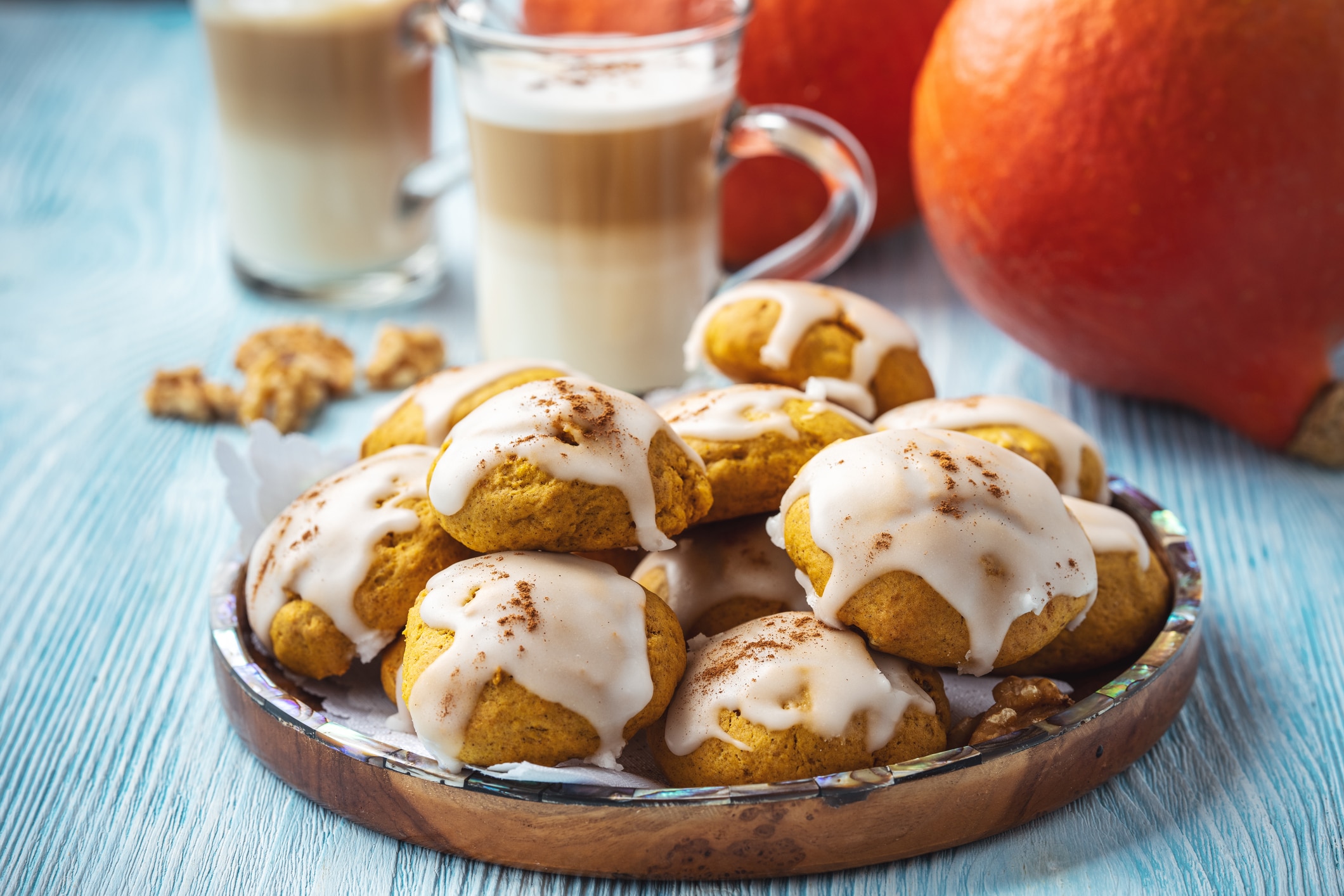Plate Of Brown Butter Cookies With Pumpkin And Icing On A Blue Wooden Table, Topped With Cinnamon And Served Beside Glasses Of Creamy Coffee And Fresh Pumpkins