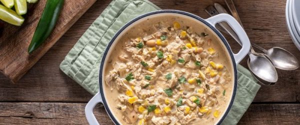 Instant Pot White Chicken Chili_Resized_Pam Higgins Instant Pot White Chicken Chili in Handled Enamelware Bowl on a Wooden Plank Tabletop With a Linen Napkin, Tortilla Chips and Lime Wedges Nearby
