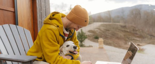 Concept of Is Cold Weather Bad for Your Lungs Represented by Guy in Orange Hat Holding Dog While Working on Laptop Outdoors in Autumn