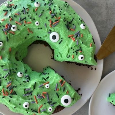 Monster Bundt Cake With Green Frosting, Candy Eyeballs and Halloween Sprinkles on White Plate
