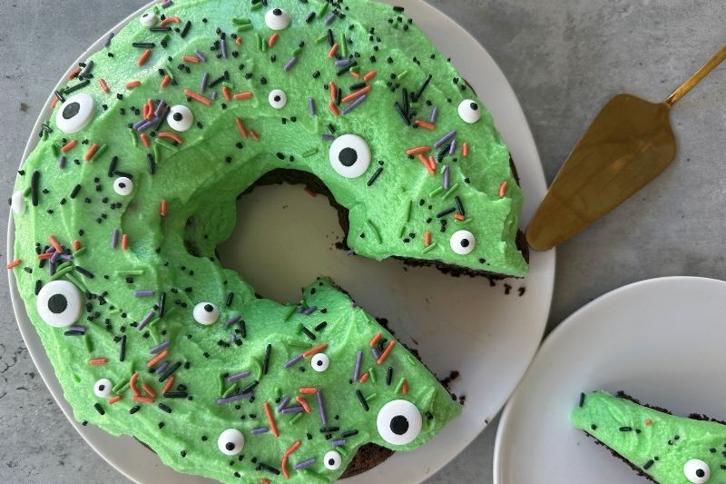Monster Bundt Cake With Green Frosting, Candy Eyeballs and Halloween Sprinkles on White Plate