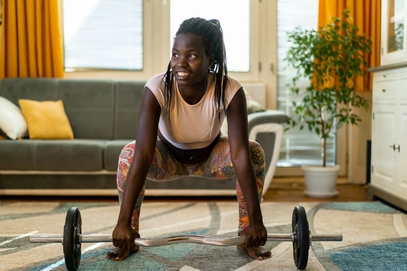 Woman Smiling While Lifting Barbell During Home Workout