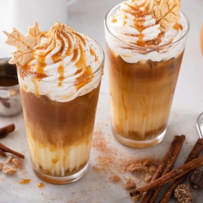 Two Iced Pumpkin Caramel Lattes Are Topped With Whipped Cream, Caramel Drizzle and Little Leaf Cookies.