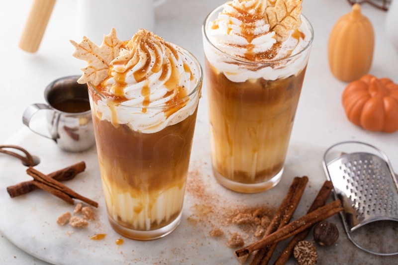 Two Iced Pumpkin Caramel Lattes Are Topped With Whipped Cream, Caramel Drizzle and Little Leaf Cookies.