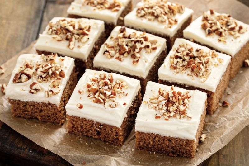 Sliced Squares of Pumpkin Sheet Cake with Creamy Frosting and Chopped Nuts on Top