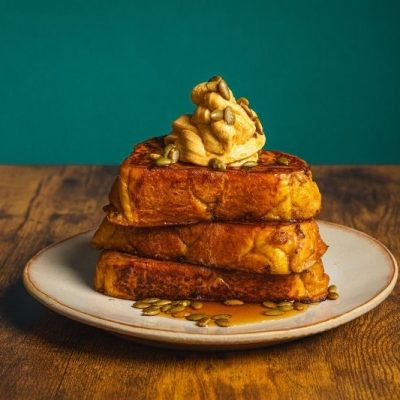 Pumpkin Spice French Toast With Whipped Pumpkin Butter Stacked on a Plate With Maple Syrup and Pumpkin Seeds