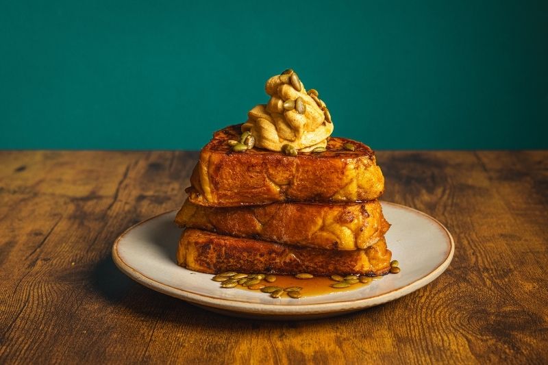 Pumpkin Spice French Toast With Whipped Pumpkin Butter Stacked on a Plate With Maple Syrup and Pumpkin Seeds