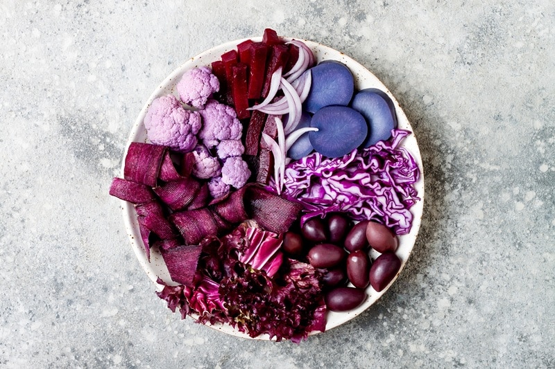 A Plate is Filled With Purple Fruits and Vegetables, Including Beets, Cauliflower, Cabbage, Grapes, Onion and Potato.