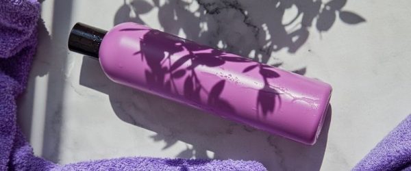 Purple Shampoo Bottle on White Marble Surface with Purple Towel and Leaf Shadows