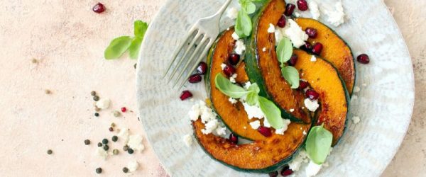 Golden Wedges of Oven Roasted Acorn Squash Scattered with Sage Leaves & Feta Cheese on a Textured Round Plate with a Waiting Fork