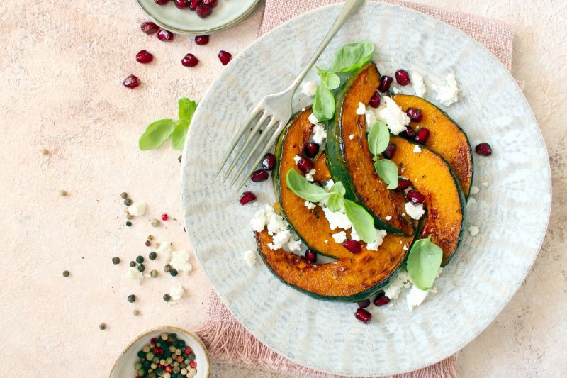 Golden Wedges of Oven Roasted Acorn Squash Scattered with Sage Leaves & Feta Cheese on a Textured Round Plate with a Waiting Fork