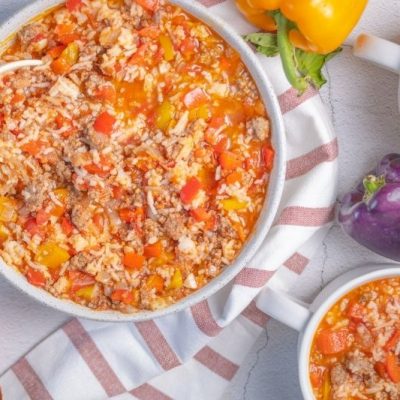 Bowl And Mugs Of Hearty Stuffed Pepper Soup Made With Ground Beef, Rice, Diced Tomatoes, And Colorful Bell Peppers, Served On A Striped Towel With Fresh Peppers