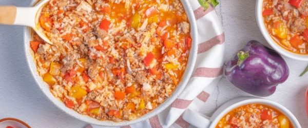 Bowl And Mugs Of Hearty Stuffed Pepper Soup Made With Ground Beef, Rice, Diced Tomatoes, And Colorful Bell Peppers, Served On A Striped Towel With Fresh Peppers