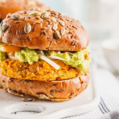 Two Sweet Potato Burgers with Guacamole, Tomato and Onion on Seed-Topped Whole Grain Buns