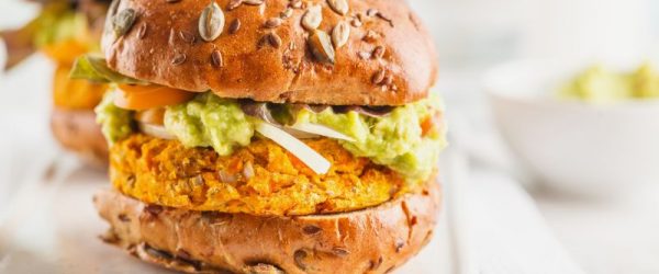 Two Sweet Potato Burgers with Guacamole, Tomato and Onion on Seed-Topped Whole Grain Buns