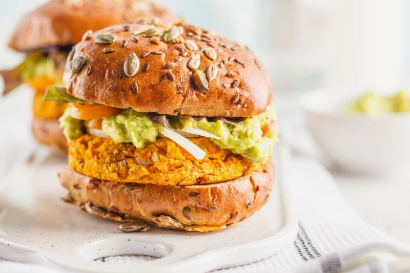 Two Sweet Potato Burgers with Guacamole, Tomato and Onion on Seed-Topped Whole Grain Buns