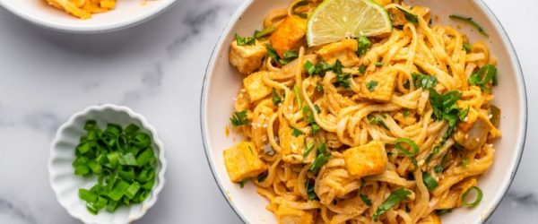 A Bowl of Thai Red Curry Noodles with Crisped Tofu and Green Onions on a Marble Counter