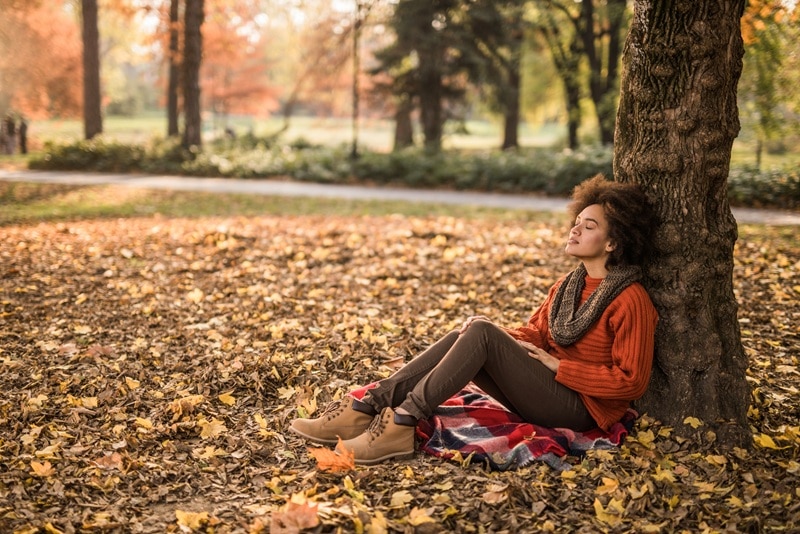 A Woman Sits Under a Tree Peacefully With Her Eyes Closed, Representing the Power of Silence.